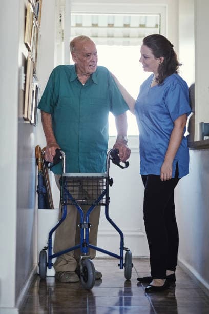 Caregiver supporting an older man as he walks with a walker